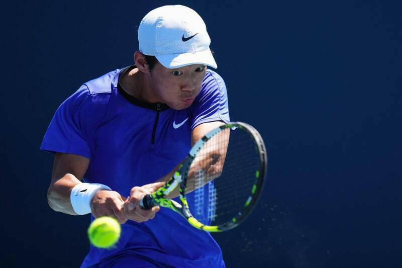 台灣網球選手曾俊欣專注回擊來球，於比賽中使出雙手反拍動作，身穿藍色球衣與白色帽子。