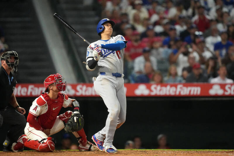 道奇隊大谷翔平在比賽中全力揮棒，球飛向外野，天使隊捕手與主審在後方觀察球的動向。