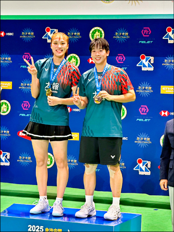 台灣女雙選手謝沛珊與洪恩慈在2025年澳門羽球公開賽奪冠後合影留念，兩人手持金牌站上頒獎台並比出勝利手勢。