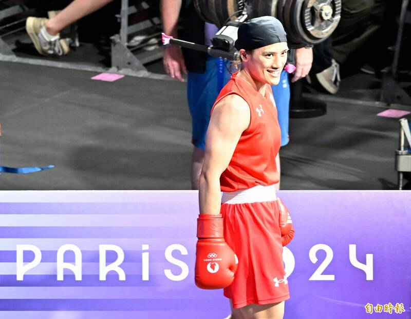 瑞士拳擊女將珍妮在巴黎奧運場邊微笑，身穿紅色拳擊服與手套，準備迎戰對手。