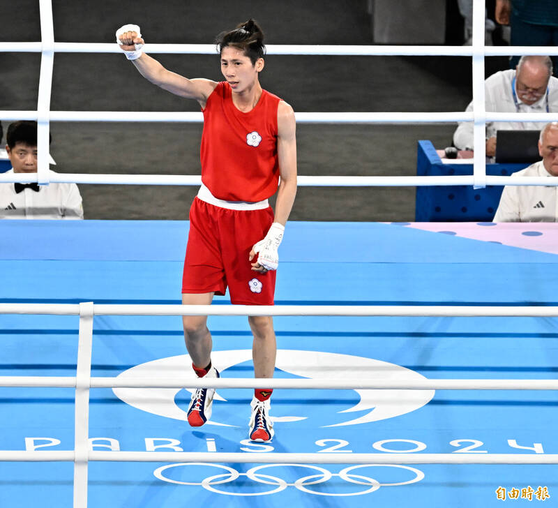 台灣拳擊女將林郁婷在巴黎奧運拳擊賽場上舉手慶祝勝利，身穿紅色拳擊服，神情自信。