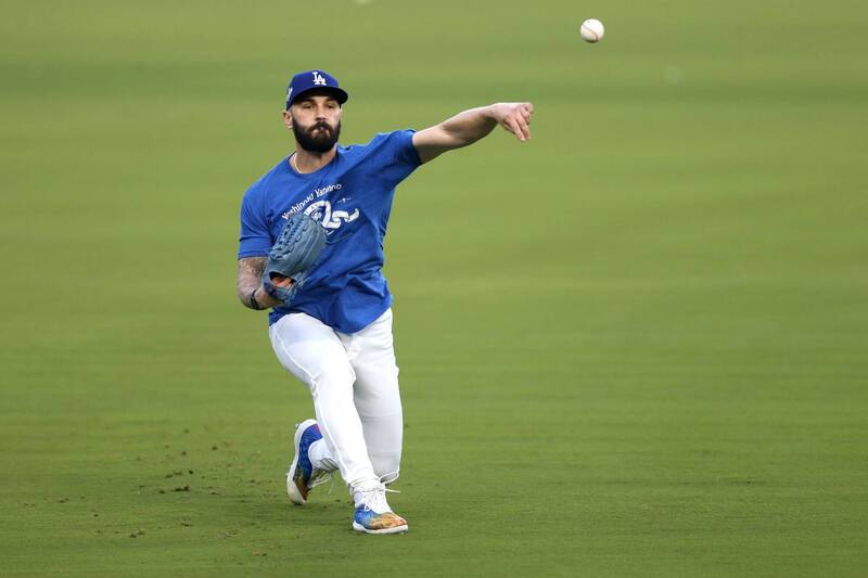 一名穿著藍色上衣與白色球褲的棒球選手在外野草地上做傳球動作，呈現單膝跪地的姿勢，專注完成練習。