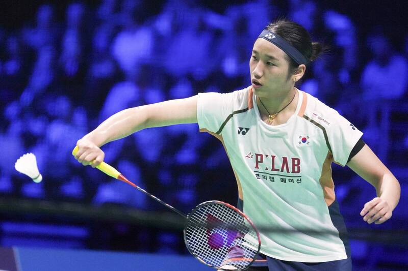 「一名南韓女子羽球選手在場上專注揮拍回擊羽球，動作流暢，背景為比賽觀眾席的燈光效果。」