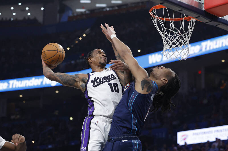 一名身穿白色球衣的籃球員在禁區高舉球準備進攻，另一名藍色球衣防守者起跳試圖封阻，畫面呈現激烈對抗。