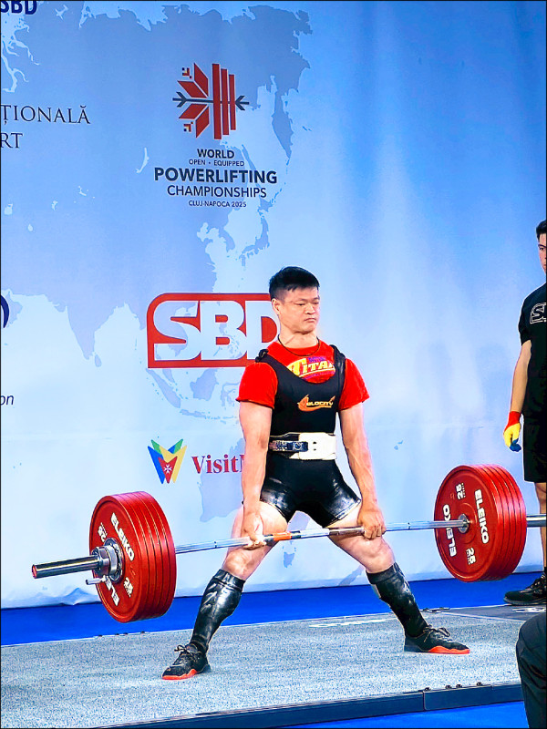 台灣健力選手在世界公開裝備健力錦標賽中進行硬舉，以全力拉起紅色槓鈴展現強大爆發力的比賽畫面。