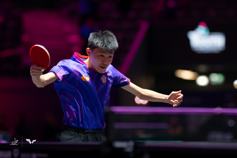 一名身穿紫色球衣的桌球選手在比賽中全神貫注揮拍進攻，背景為燈光昏暗的室內球場。