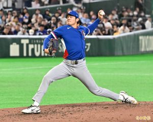 台灣 20 歲旅美左投新星林維恩在檔案 "phpsbXG02.jpg" 中，身穿台灣國家隊（中華隊）經典的寶藍色比賽球衣，左胸繡有紅白藍三色的「CT」官方隊徽，內搭寶藍色長袖緊身衣，頭戴印有白色「CT」標誌的寶藍色國家隊棒球帽。他正身處於台北大巨蛋或東京巨蛋的綠色人工草皮投手丘上，展現其帥氣且延伸性極佳的左投出手投球動作。他的右腳高高踏向前方、上身舒展，左手持球高高舉起準備全力將球投出，右手則戴著黑底配紅色縫線的棒球手套護在身側，神情顯得有些咬牙用力的專注神態，背景則是黑壓壓坐滿觀眾的內野看台與帶有「Trust」字樣的綠色全壘打牆。