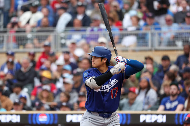 洛杉磯道奇隊日籍巨星大谷翔平身穿藍色「Los Angeles」客場 17 號球衣，手臂戴著深藍色與白色防護具，雙手戴著白、紅、藍三色線條的打擊手套。他在打擊區內將黑色球棒高舉過頭，身體微蹲，眼神無比專注地凝視前方投手丘，展現極具壓迫感的打擊準備姿勢。