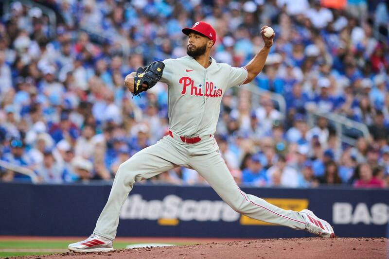 費城人隊王牌左投桑契斯（Cristopher Sánchez）身穿灰色「Phillies」紅色草寫字樣的客場比賽球衣、紅色球帽。他在投手丘上展現大跨步的左投投球連續動作，右手戴著黑色 Wilson 棒球手套在胸前維持平衡，左手則將棒球高高舉起準備奮力投出，神情充滿對決打者的自信。