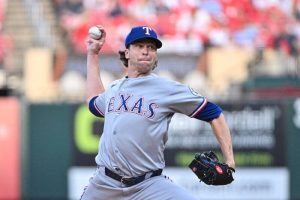 德州遊騎兵隊王牌投手德葛隆(Jacob deGrom)身穿灰色客場球衣高舉右手準備投球,本場比賽他主投5局飆出8K無失分,奪得大聯盟生涯第100場勝投。