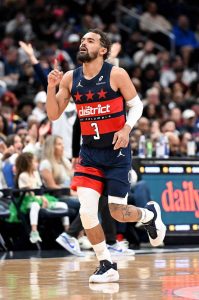 明星後衛楊恩（Trae Young）身穿華盛頓巫師隊深藍色、胸前印有紅色區塊及白色「the district OF COLUMBIA」字樣的主場 3 號球衣與白色緊身褲。他滿臉落腮鬍、神情激昂昂首走在木地板球場上，右手食指指向天空，左手臂戴著白色護袖，正與全場觀眾一同慶祝勝利。