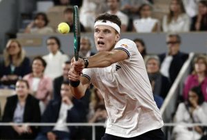 捷克網球新星門希克（Jakub Mensik）頭戴白色運動頭帶、身穿白色網球球衣，在紅土賽場上專注地雙手持拍完成一記強力的反拍回擊。