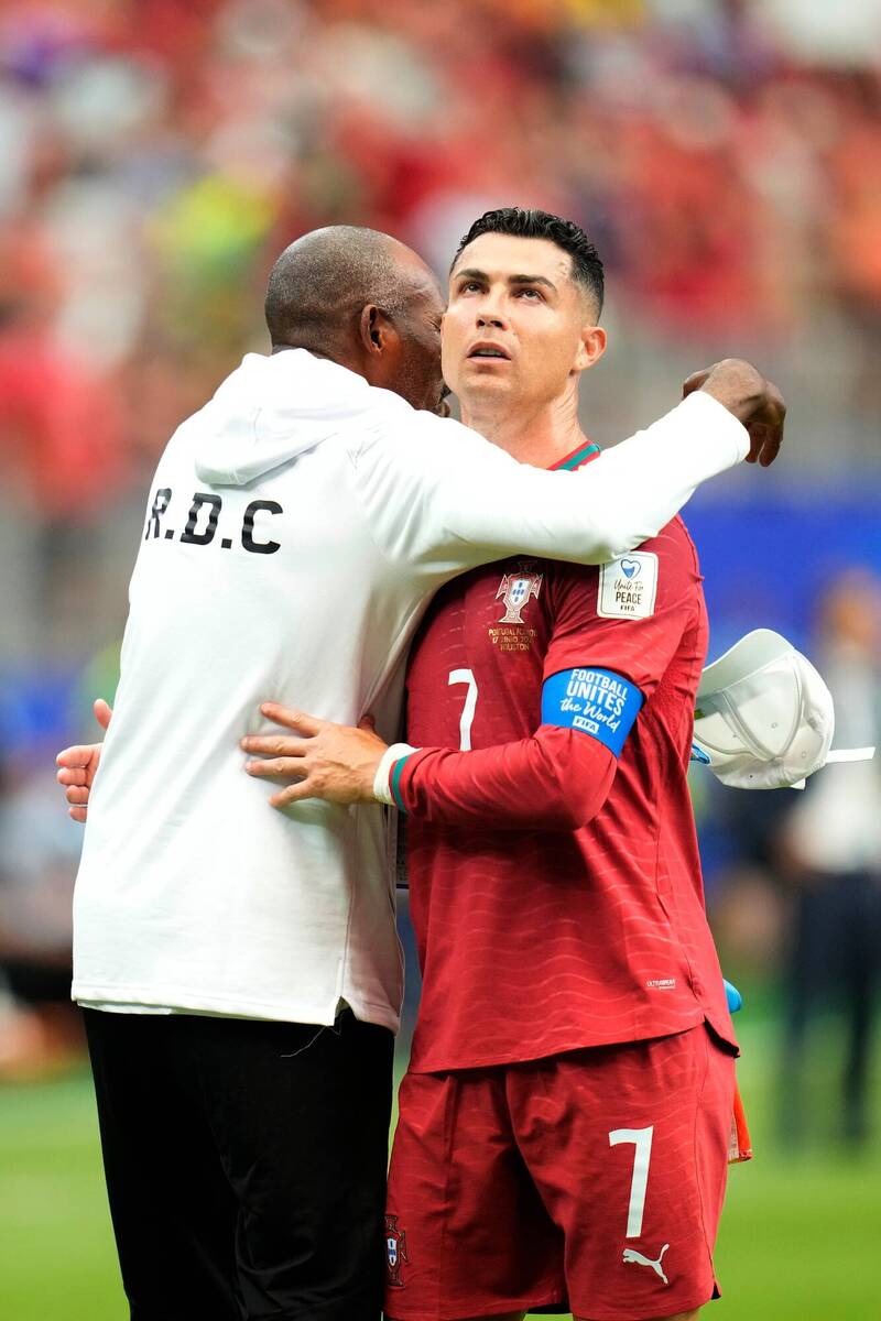 葡萄牙巨星 C 羅（Cristiano Ronaldo）身穿經典的 7 號紅色國家隊球衣，左臂戴著藍色國際足總（FIFA）隊長袖標，在球場檔案 "phpZAYHOx.jpg" 中與身穿印有「R.D.C」字樣白色運動外套的剛果隊教練或隨隊人員神情凝重地擁抱示意。
