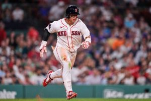 紅襪隊台灣球員鄭宗哲身穿白色「RED SOX」球衣與黑頭盔,神情專注地在棒球場上奮力奔跑。