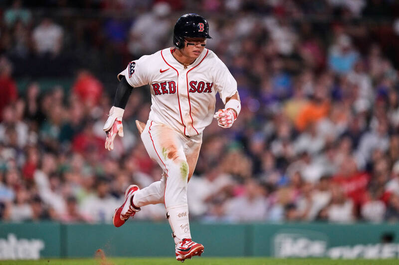 紅襪隊台灣球員鄭宗哲身穿白色「RED SOX」球衣與黑頭盔，神情專注地在棒球場上奮力奔跑。