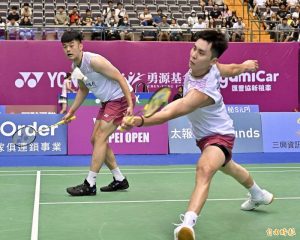 王齊麟與邱相榤身穿白色無袖球衣於羽球場上奮力進行前排與後排擊球。